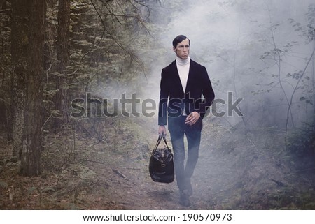 the man in a suit and with a bag in the foggy wood