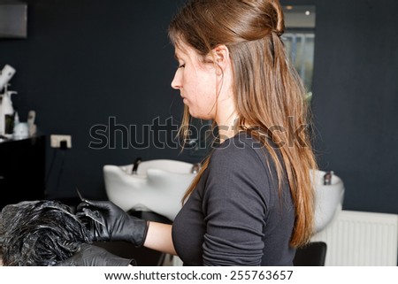 hairdresser is coloring the hair of a customer to black