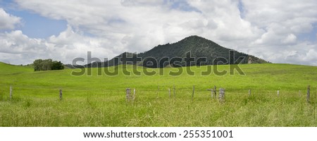 Rural Australian panorama country scene with barb wire fence line, rolling green hills, cloudy summer sky in Queensland