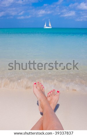 Womans feet at waters edge with sailboat