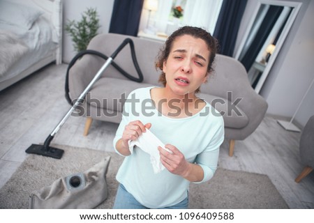 Sneezing hard. Young woman looking desperately sick while inhaling dust coming out of dust container developing allergy to dust