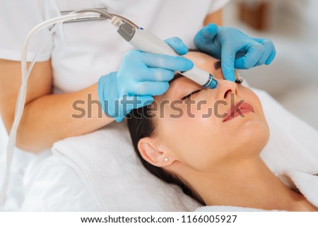Cleansing procedure. Nice pretty woman lying with her eyes closed while having a cleansing procedure on her face