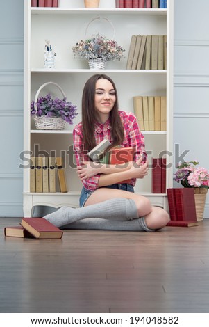 Cheerful young woman with books sitting in the room with shelves