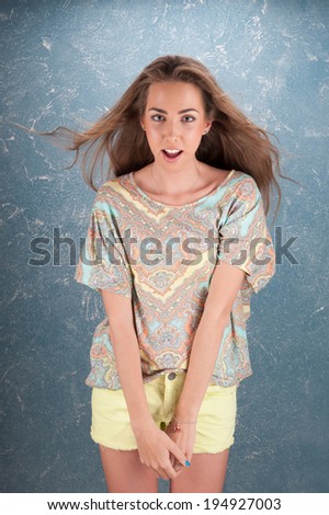 Emotional cheerful young dark-blonde woman with long hair standing in half length on creative background