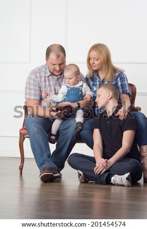 Full length family portrait with parents and two children sitting on sofa and reading a book, studio shot