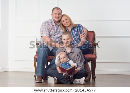 Full length family portrait with parents and two children sitting on sofa and reading a book, studio shot