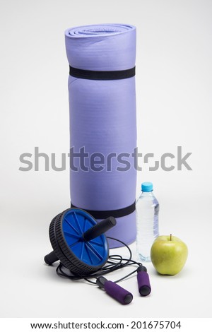 Close up image of yoga mat with skipping rope, water bottle, workout fitness exercise roller and apple closeup isolated on white background
