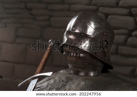 Closeup of knight armor helmet and sword on the dark stone wall background