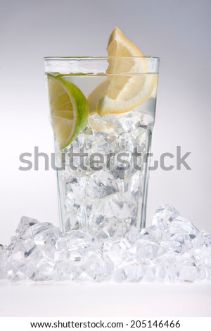 Glass of water with ice, lemon and lime surrounded by ice cubes isolated on white background