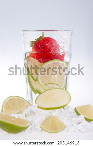 Glass of water with strawberry, lemon and lime, water splashes and droplets, surrounded by ice cubes and slices of lemon isolated on white background