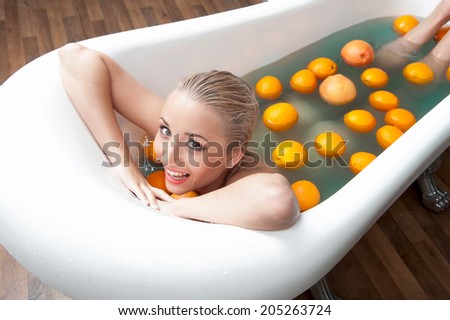 Top view portrait of sexual young blonde nude woman smiling and relaxing in the bath with oranges