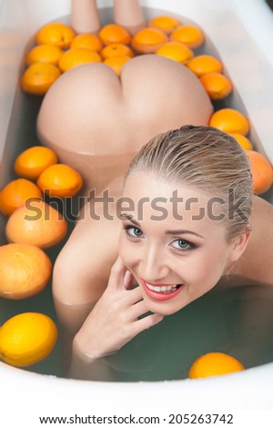 Top view portrait of sexual young blonde nude woman smiling and relaxing in the bath with oranges