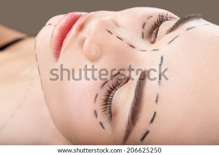 Top view portrait of beautiful young woman with perforation lines around her eyes and chin looking up before plastic surgery operation isolated on grey