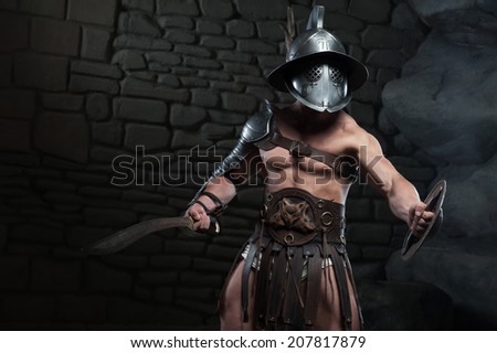 Half length portrait of warrior gladiator with muscular body in helmet holding sword on dark background. Concept of masculine power, strength