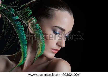 Beautiful brunette young woman with peacock style make-up and peacock feather, sideview  portrait isolated on black background