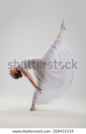 Full length portrait of young and beautiful modern style ballet dancer jumping lifting leg up isolated on white background, studio shot