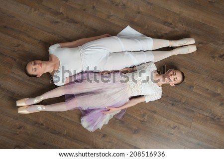 Two beautiful young ballet dancers posing, lying on the wooden floor of ballet hall, top view portrait