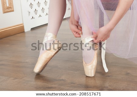 Closeup portrait of two young beautiful ballet dancers sitting on sofa, tying up ballet shoes in classical interior