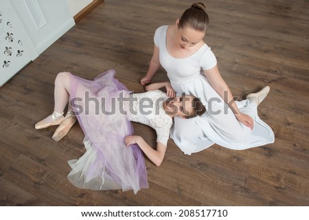 Two beautiful young ballet dancers posing, lying on the wooden floor of ballet hall, top view portrait