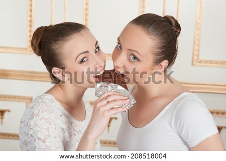 Two young beautiful ballet dancers eating a bar of chocolate in classical interior. Concept of diet, wellness