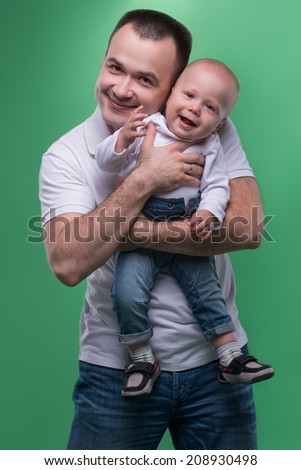 Waist up portrait of happy smiling handsome father and cute son baby boy in white shirt and jeans posing, family concept, isolated on green