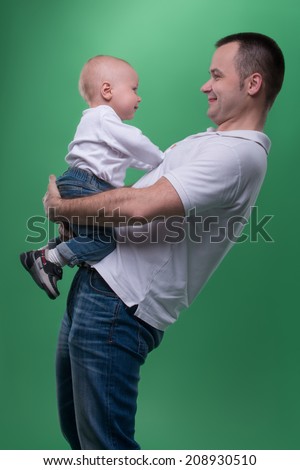 Portrait of happy smiling handsome father and his son baby boy in white polo shirt looking at each other, family concept, isolated on green background