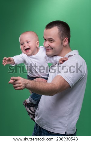 Portrait of happy smiling handsome father and cute son baby boy in white shirt and jeans reaching something, stretching forward, family concept, isolated on green