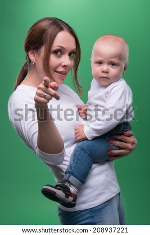 Half length portrait of young attractive Caucasian mother and cute baby pointing at camera and smiling, isolated on green