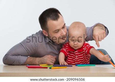 Closeup portrait of young handsome Caucasian father drawing with his cute toddler son, dad is pointing at something, isolated on white