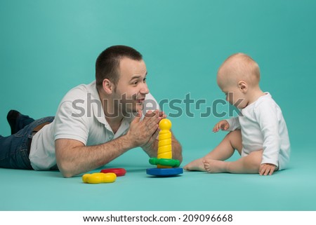 Happy handsome smiling Caucasian father playing with his son baby boy, picking up pyramid circles, isolated on blue. Family fun concept