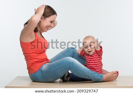 Portrait of young attractive Caucasian mother sitting face to face to her cute toddler son playing with hands on head, lifestyle fun concept, isolated on white