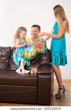 Full length portrait of happy adorable Caucasian family, little daughter and beautiful blonde mother looking into present package, smiling father hugging girl, at home