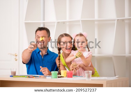 Family portrait, happy caucasian father, beautiful mother and daughter posing while painting a picture with watercolours, handsome father pointing at camera, interior shot