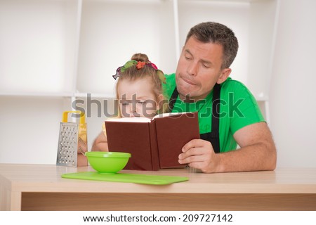 Half length portrait of happy funny handsome man and his cute little daughter wearing apron and preparing to cook with cooking book, grater and bowl, studio shot