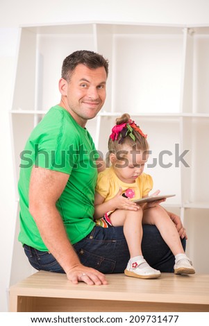 Half-length portrait of happy smiling father and child using electronic tablet at home sitting on desk
