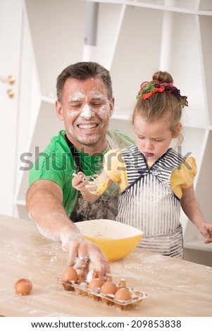 Funny portrait of cute little daughter with handsome father cooking pastry, making dough