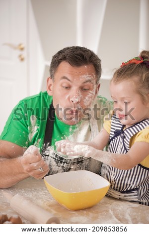 Half-length portrait of cute little daughter with happy handsome father cooking pastry, mixing flour and having fun