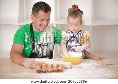 Half-length portrait of cute little daughter with happy handsome father cooking pastry, mixing flour and having fun. Top view