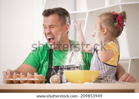 Half-length portrait of cute little daughter with happy handsome father cooking pastry, mixing flour and having fun