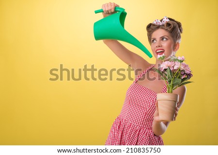 Half length portrait of beautiful sexy girl with pretty smile wearing dress in pin-up style watering flowers with can, isolated on yellow
