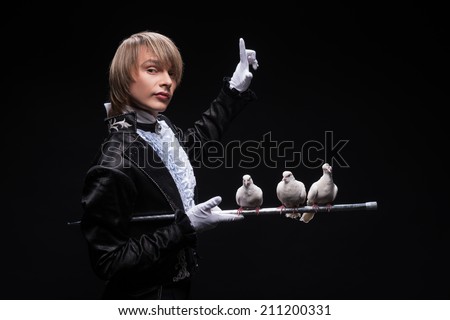 Half-length portrait of fair-haired matchless juggler wearing interesting black costume and white shirt standing aside holding three pouters on the silver stick. Isolated on black background