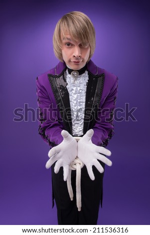 Half-length portrait of juggler wearing splendid violet jacket white shirt and black pants standing with tied hands. Isolated on blue background