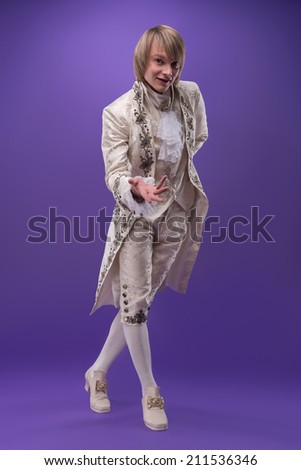 Full-length portrait of handsome fair-haired juggler wearing great white costume invited us to see his performance. Isolated on violet background