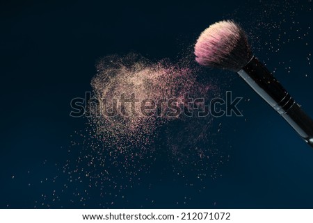 Horizontal close-up photo of professional   black make-up brush with pink powder in motion isolated on blue background with copy place
