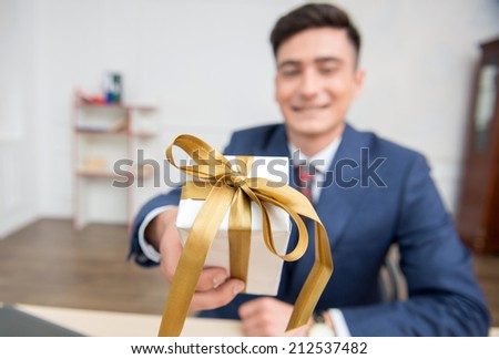 Close-up selective focus on a gift box in hands of young businessman in office working on his computer,showing a box to the camera