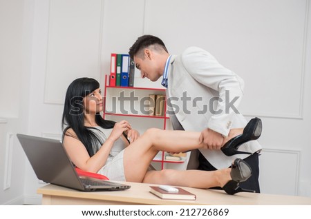Side view portrait of young business couple in passion looking to each other while woman sitting on the chair at the desk and man holding her leg with pas