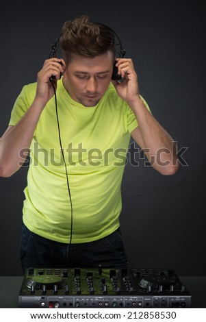 DJ playing music. Confident young DJ with stylish haircut and headphones at work spinning on mixer looking down while standing isolated on dark background