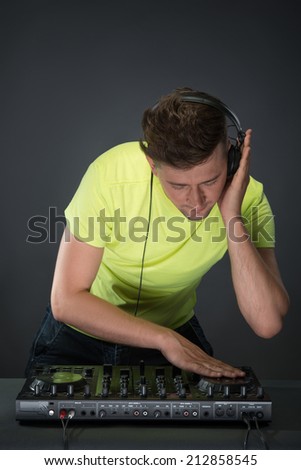 Half-length portrait of confident young DJ with stylish haircut and headphones on head spinning and mixing music on mixer while standing isolated on dark background