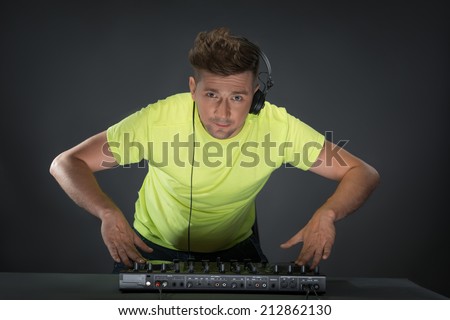 Half-length portrait of confident young DJ with stylish haircut and headphones on head spinning and mixing music on mixer while standing isolated on dark background
