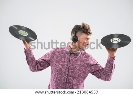 Half-length closeup portrait of excited young DJ with stylish haircut, bow tie and headphones posing with two vinyl records looking sideways isolated on white background